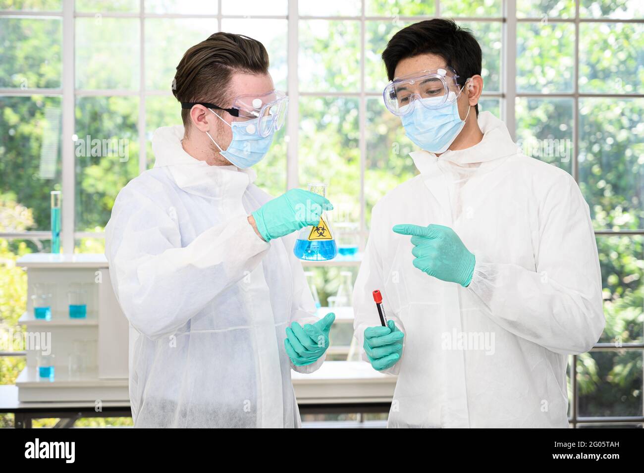 Couple de scientifiques mâles portant une combinaison de protection tenant le vaccin et travaillant avec de nombreux équipements de laboratoire pour la recherche de vaccins en laboratoire. Recherche médicale Banque D'Images