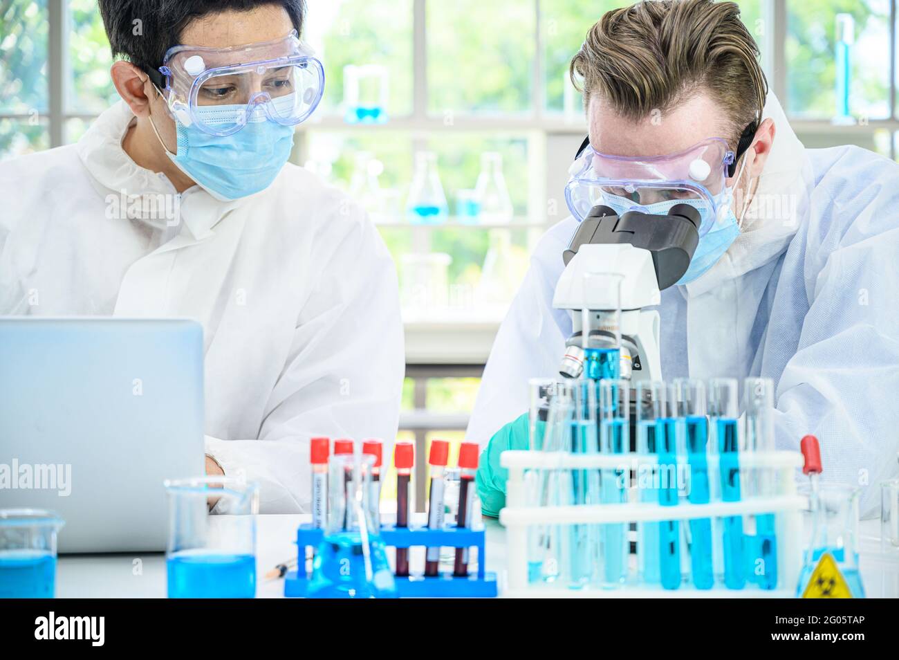 Couple scientifique mâle portant une combinaison de protection travaillant avec de nombreux équipements de laboratoire et ordinateur portable pour la recherche de vaccins en laboratoire. Traitement médical Banque D'Images