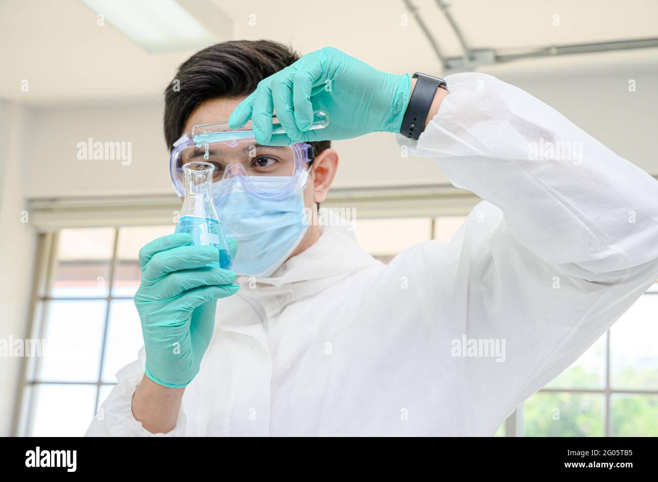 Un scientifique mâle porte une combinaison de protection pour le maintien d'un bécher ou d'un tube avec prélever du liquide à l'intérieur et travailler avec de nombreux équipements de laboratoire pour recherche en laboratoire Banque D'Images