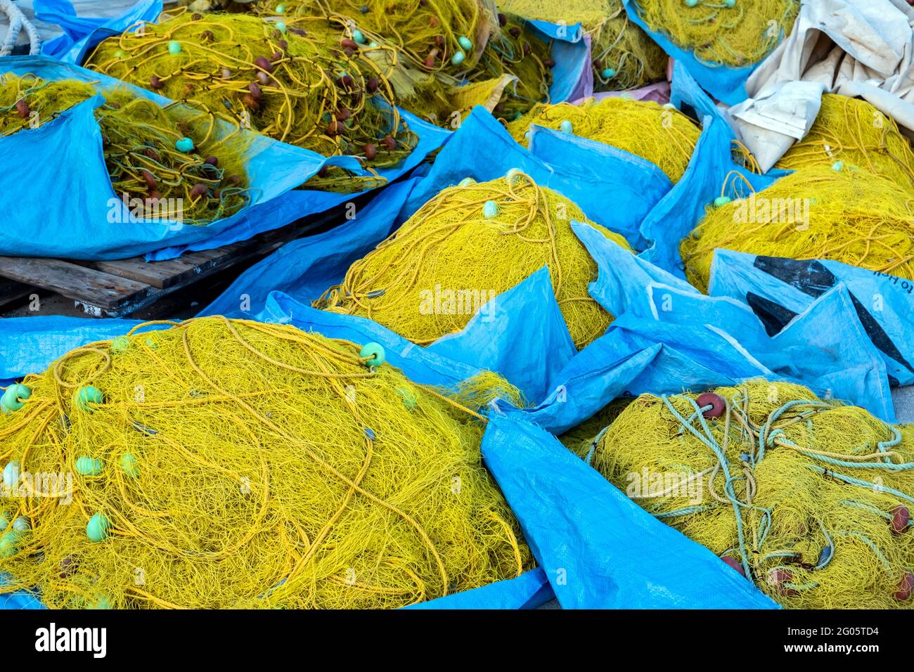 Filets de pêche séchant sous le soleil dans le port de pêcheur. Les filets de pêche de couleur jaune s'empilent sur le fond bleu des sacs. Matériel de pêche Banque D'Images