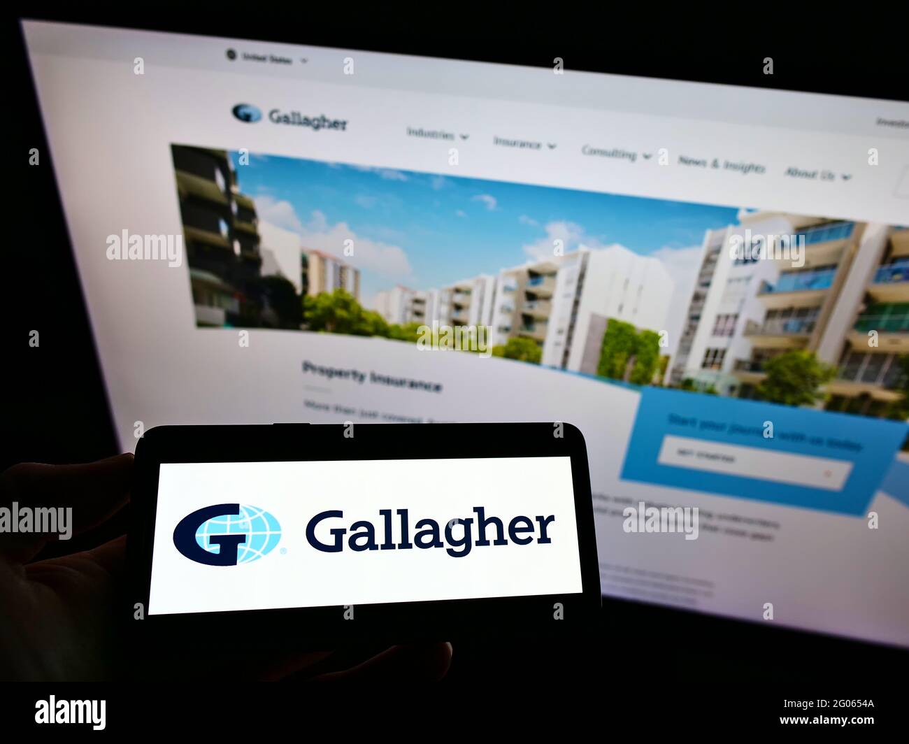 Personne tenant un téléphone portable avec le logo de la compagnie d'assurance américaine Arthur J. Gallagher Co. À l'écran en face de la page Web. Mise au point sur l'affichage du téléphone. Banque D'Images