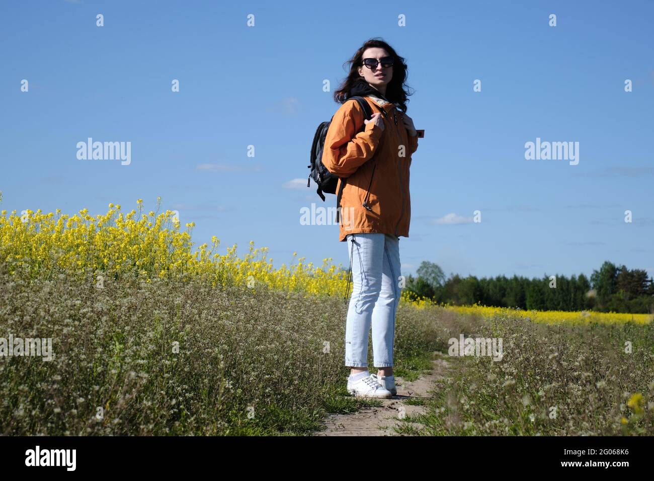 Une fille marche le long d'une route rurale le long d'un pré avec des fleurs. Sortir de la ville. Temps ensoleillé. Prairie avec fleurs Banque D'Images