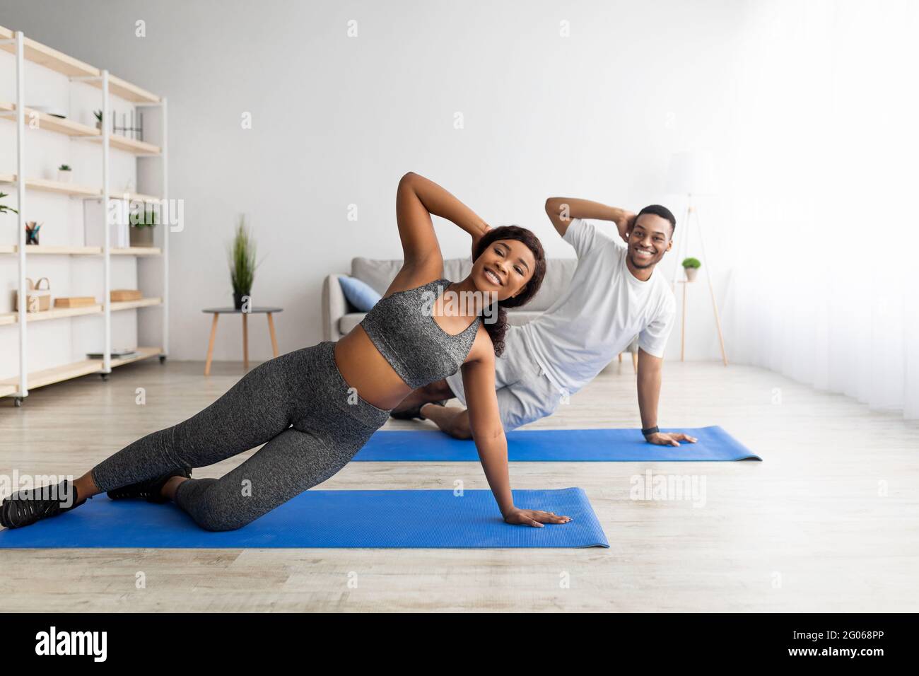 Joyeux couple noir debout sur une planche latérale sur des tapis de yoga à la maison, espace de copie Banque D'Images