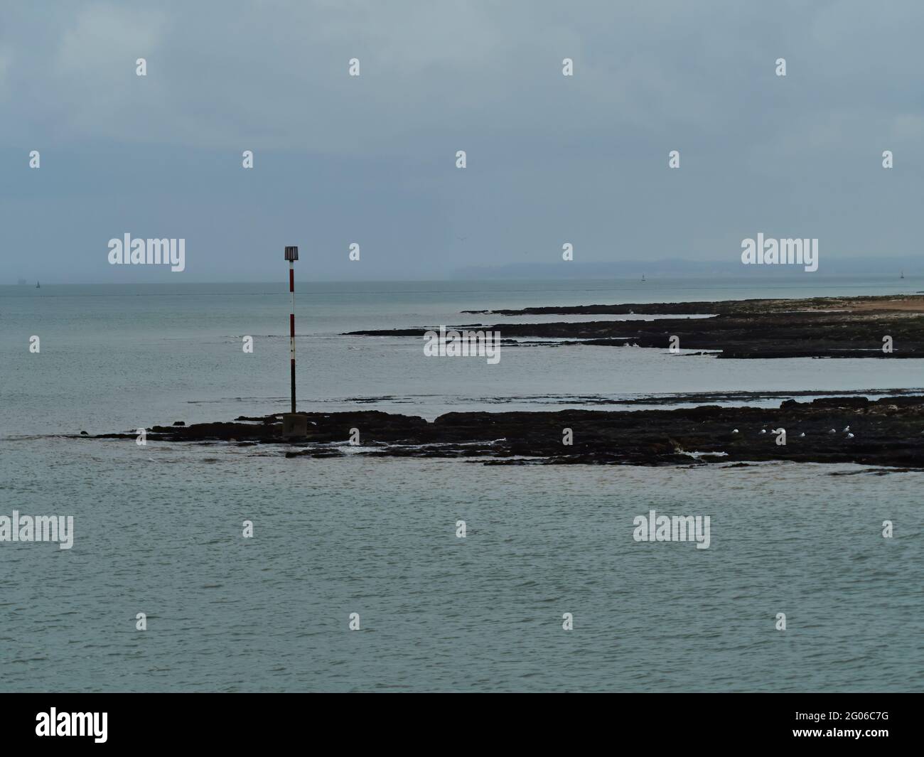 Une vue imprenable le long de la côte de Broadescaliers, avec une mer légèrement ondulée autour d'un marqueur d'avertissement sur un affleurement rocheux et des falaises lointaines à l'horizon. Banque D'Images