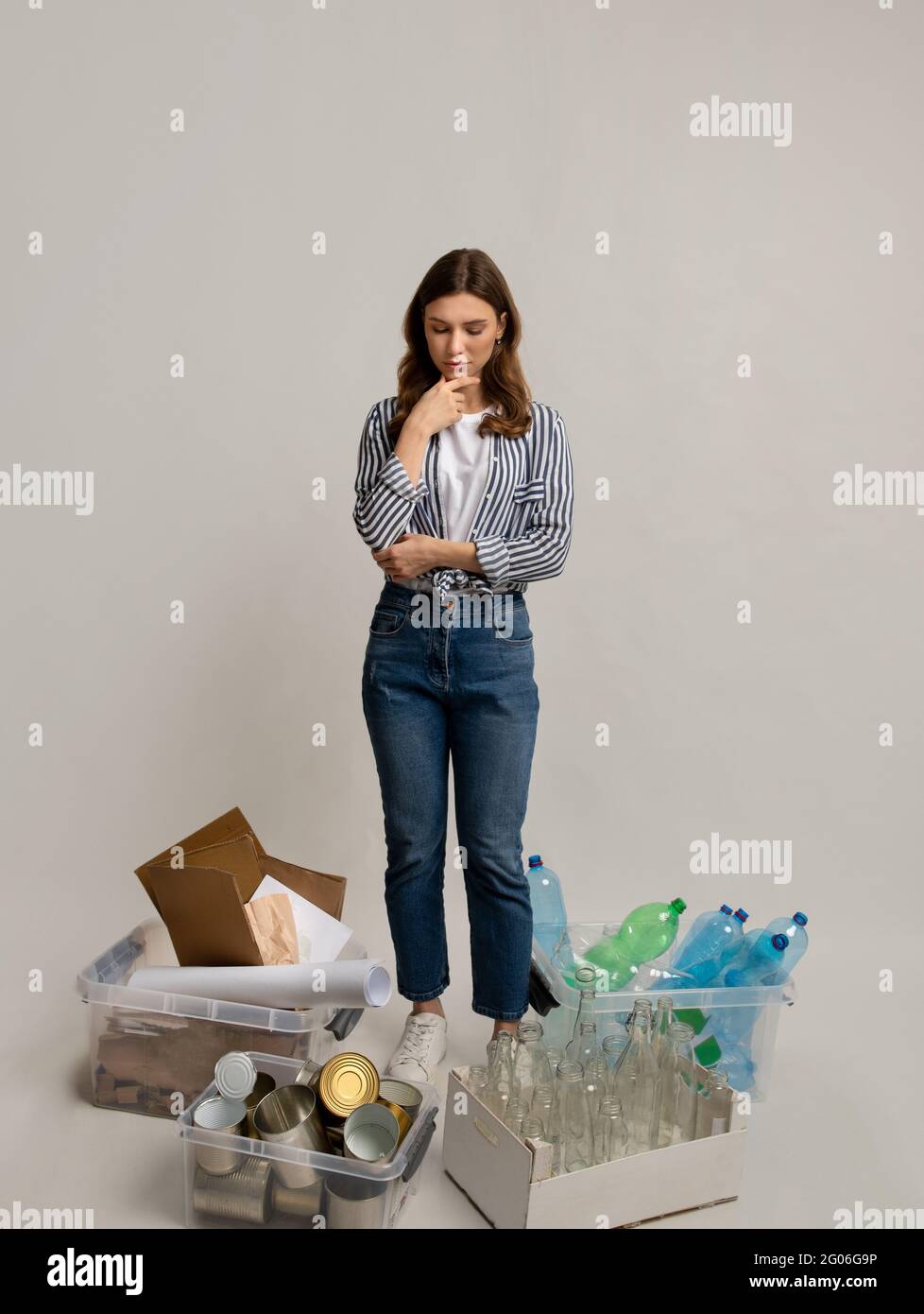 Jeune femme pensive regardant des conteneurs avec des déchets triés autour d'elle Banque D'Images