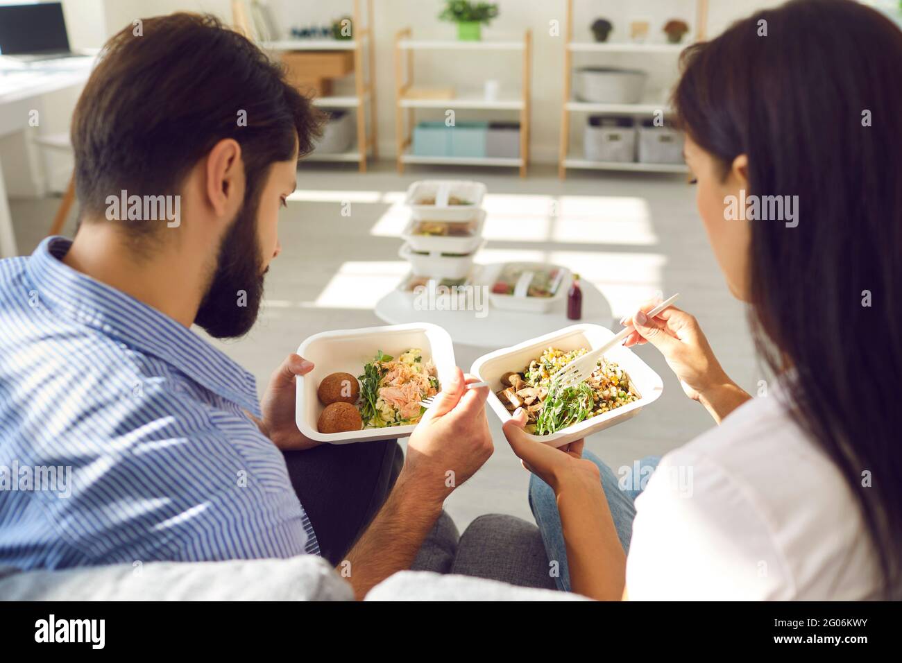 Jeune couple homme et femme travailleurs de bureau assis et appréciant une commande saine de nourriture en boîte Banque D'Images