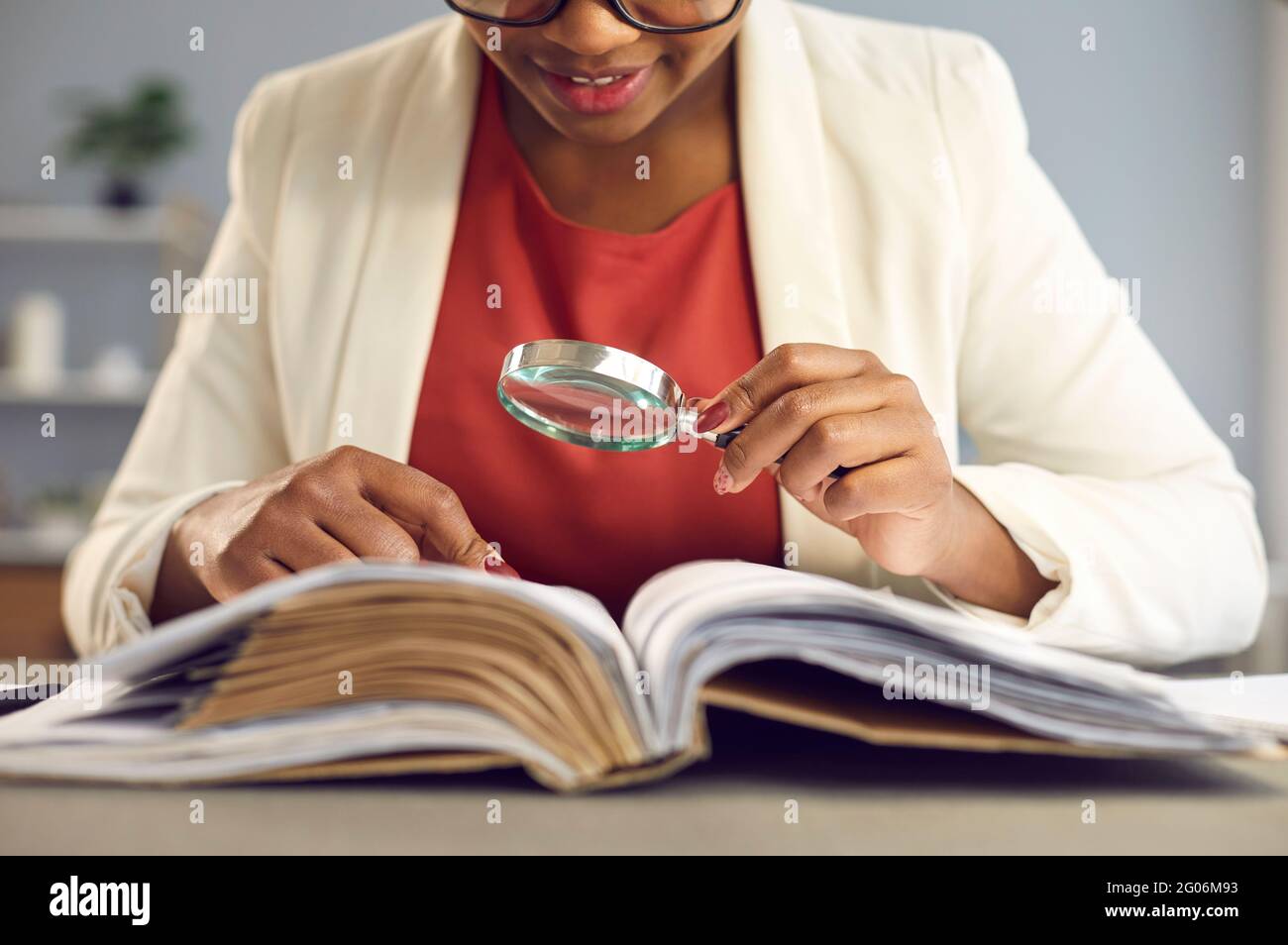 Femme avec une loupe assise à un bureau et à la recherche d'informations dans un livre Banque D'Images