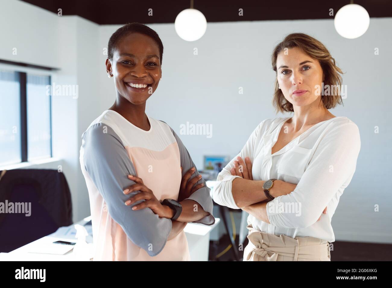 Deux femmes d'affaires souriantes et diverses debout avec les bras croisés au travail Banque D'Images