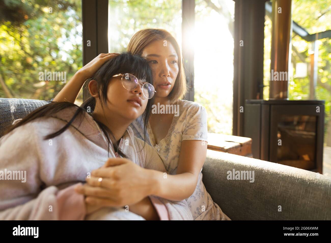 Portrait d'une triste femme asiatique avec sa fille embrassant assis sur un canapé Banque D'Images