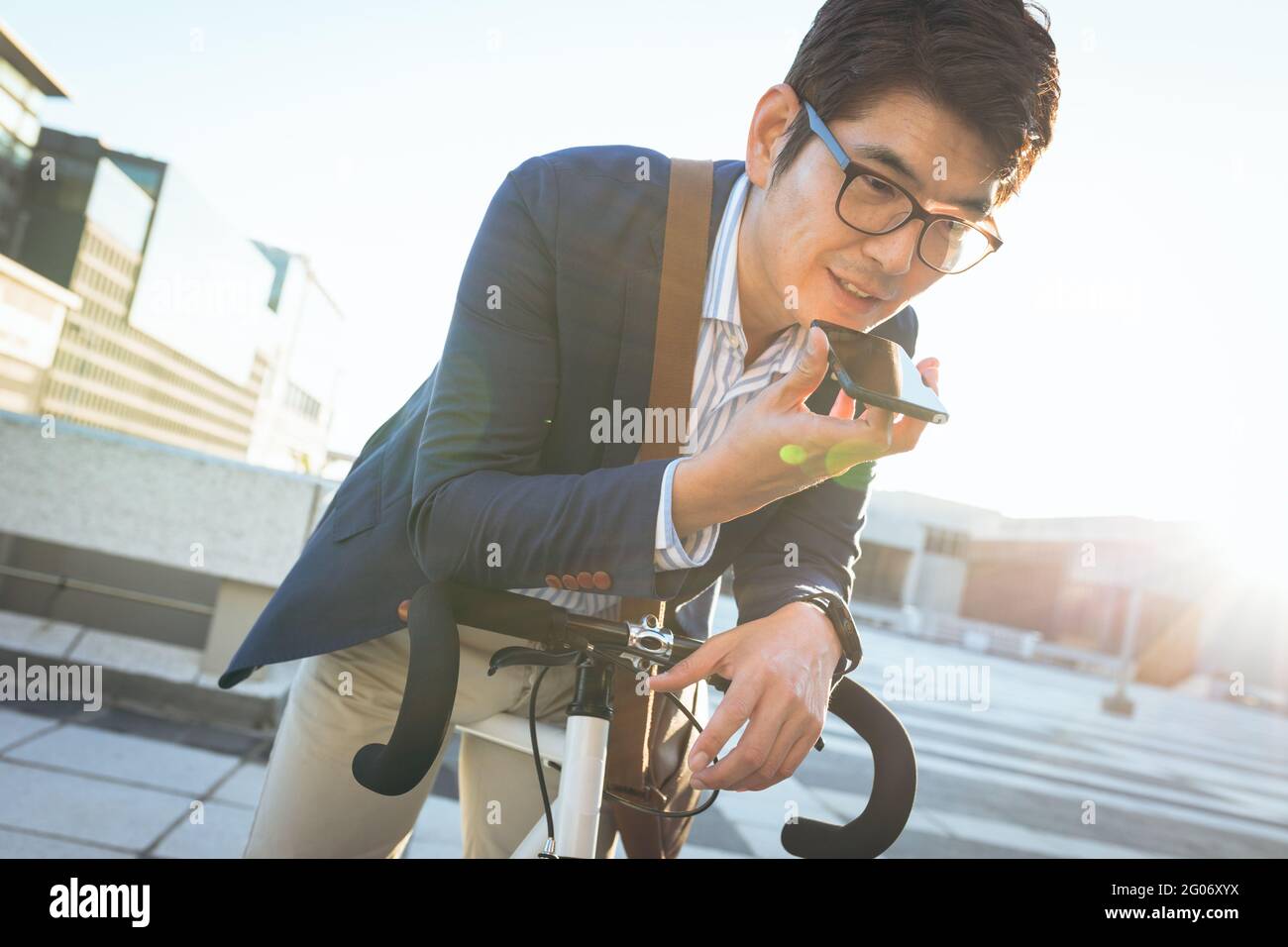 Milieu de section de l'homme d'affaires asiatique parlant sur smartphone penchée sur le vélo dans la rue de ville Banque D'Images