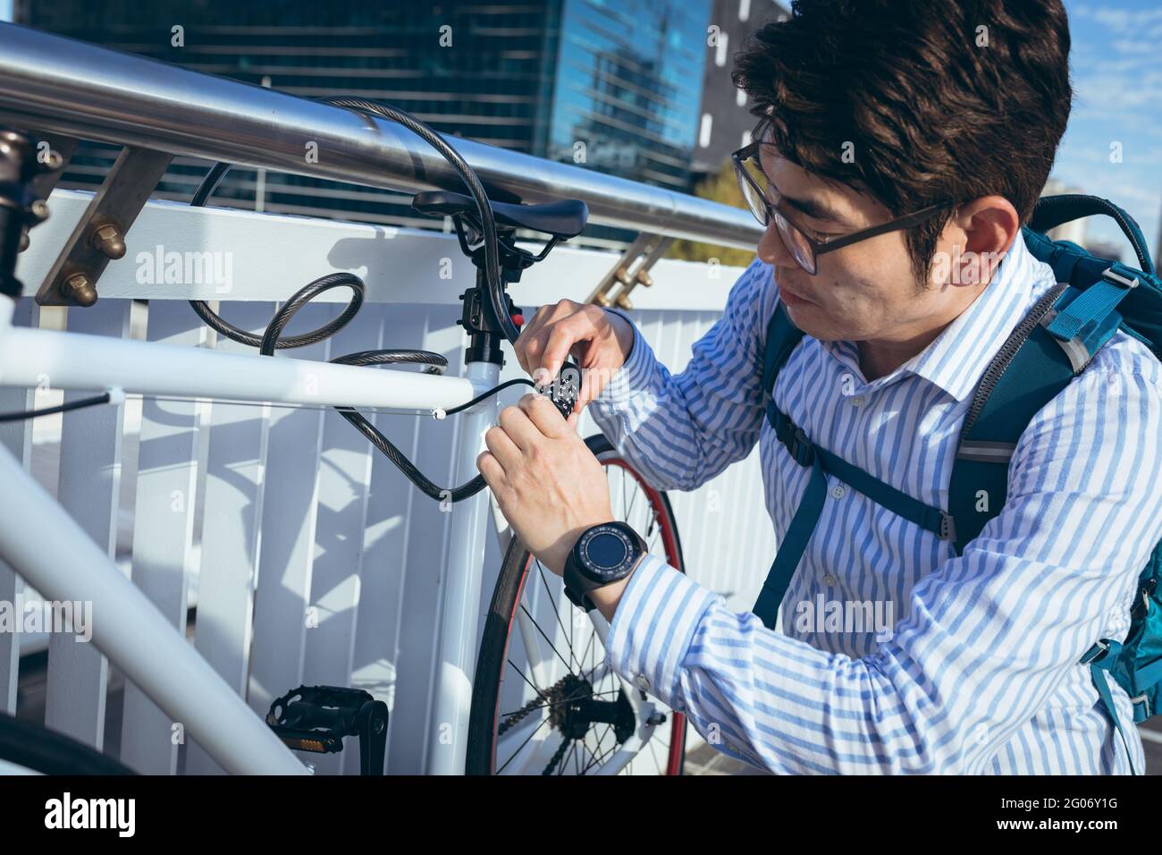 Homme d'affaires asiatique bloquant le vélo sur les rampes dans la rue de la ville avec des bâtiments modernes en arrière-plan Banque D'Images