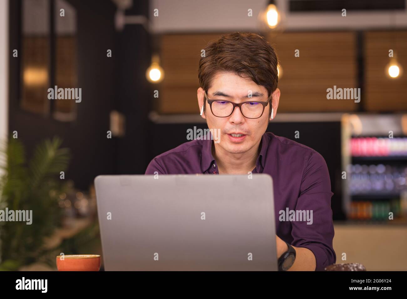 Homme d'affaires asiatique utilisant un ordinateur portable et des écouteurs sans fil dans un café Banque D'Images