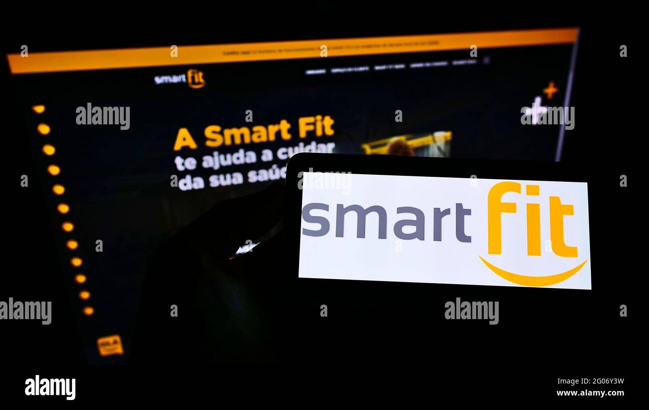 Personne tenant un smartphone avec le logo de l'opérateur brésilien de studio de fitness SmartFit à l'écran devant le site Web de l'entreprise. Mise au point sur l'affichage du téléphone. Banque D'Images