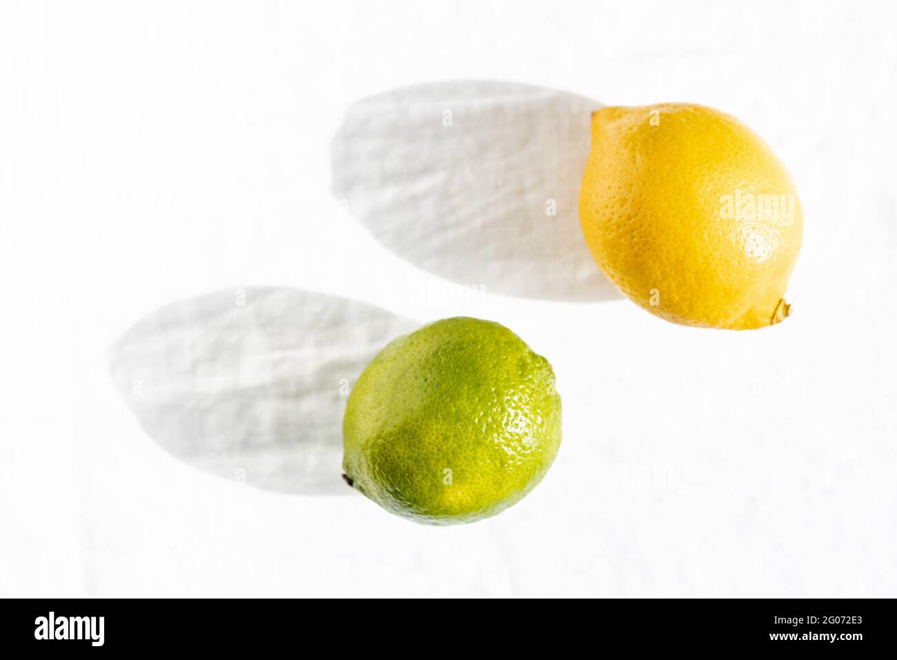 Citron et citron vert dans les lumières solaires sur fond blanc. Banque D'Images