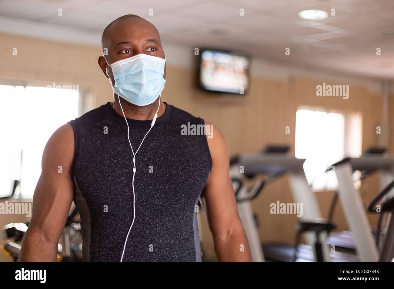 Portrait du jeune Afro-américain dans les vêtements de sport. Il est dans la salle de gym et porte un masque médical comme précaution pour éviter la contagion. Banque D'Images
