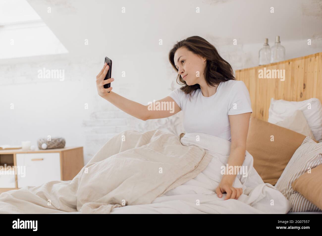 Gros plan d'une femme excitée qui rit, tient un smartphone, prend un selfie, s'amuse avec un gadget, s'allonger sur le lit, profiter de son temps libre Banque D'Images