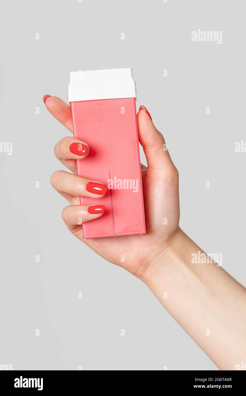 Cire chaude pour l'épilation dans les cassettes rose, bâton dans la main de femme avec des ongles rouges. Concept de tir vertical à propos de l'épilation. Banque D'Images