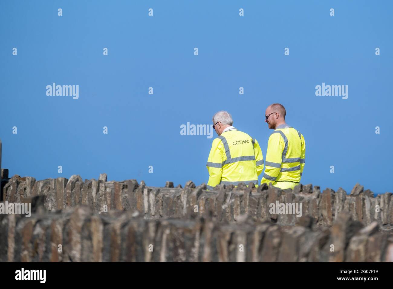Deux travailleurs de Cormac portant une veste de sécurité jaune fluorescent haute viz vue contre un ciel bleu vif. Banque D'Images