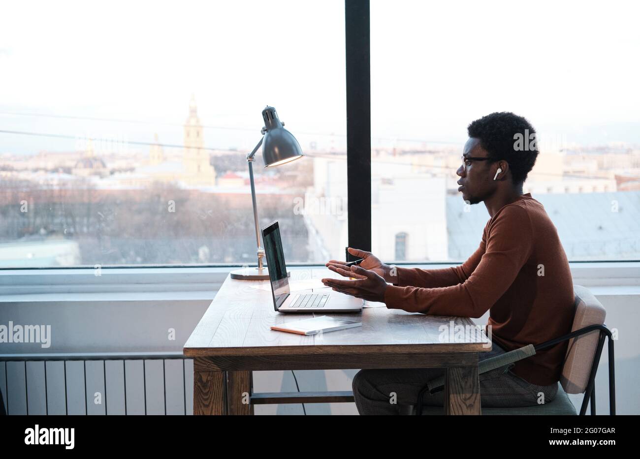 Jeune africain assis à la table et utilisant un ordinateur portable pour la réunion en ligne au bureau Banque D'Images