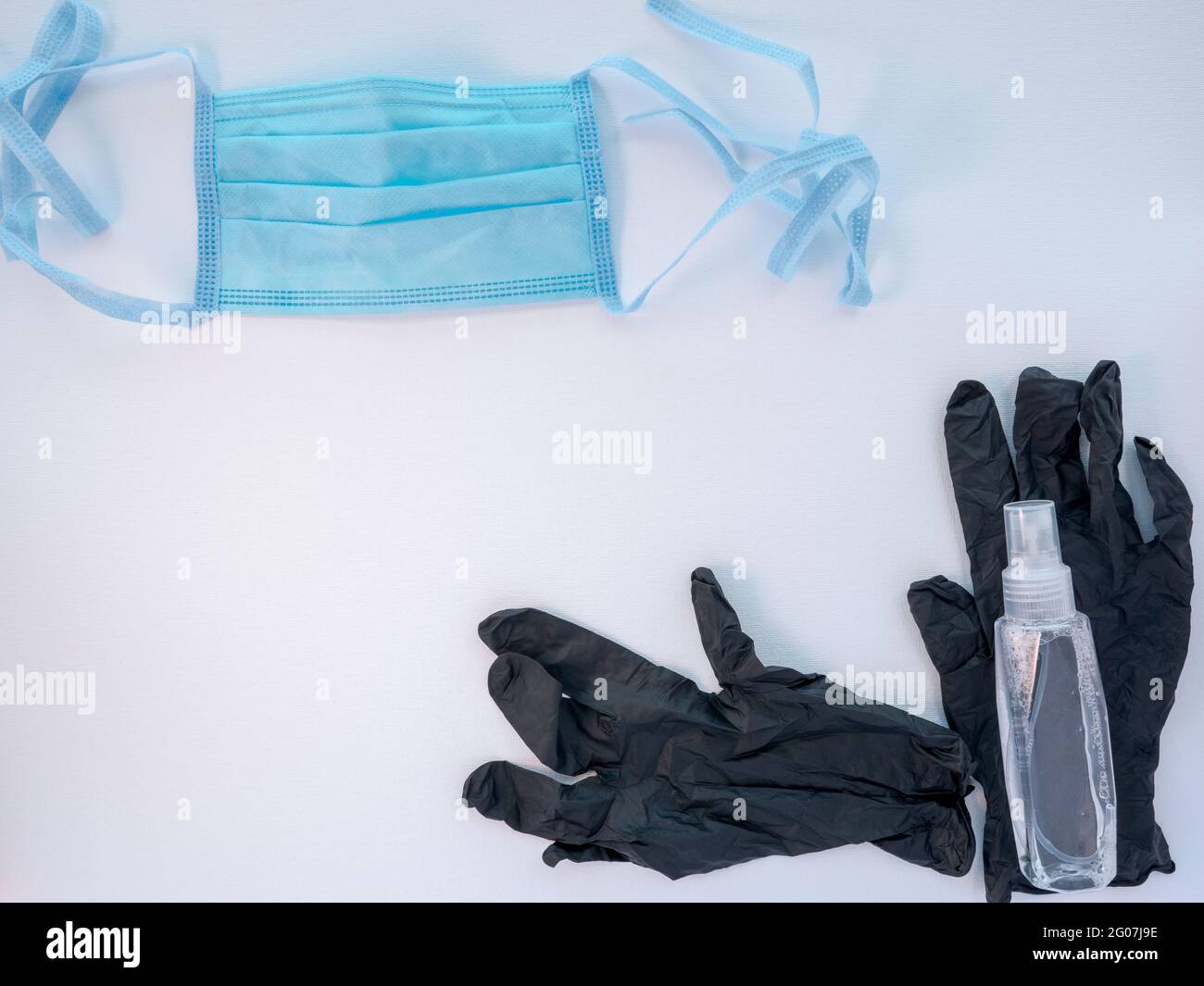 Masque de protection pour le visage médical bleu, une paire de gants en latex noir et une bouteille de désinfectant pour les mains sur fond blanc. Concept de protection antivirale. Banque D'Images