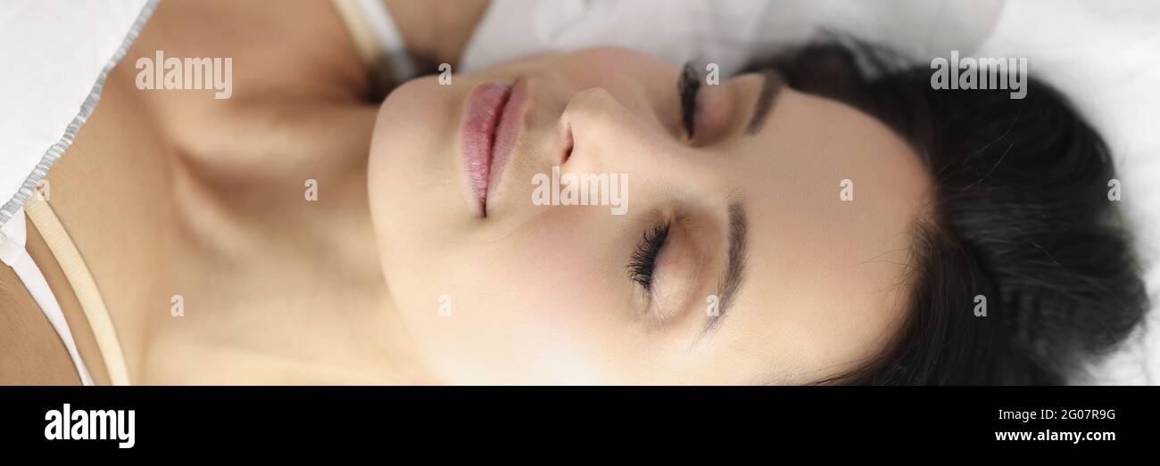 Jeune femme brune caucasienne dormant dans un lit blanc Banque D'Images