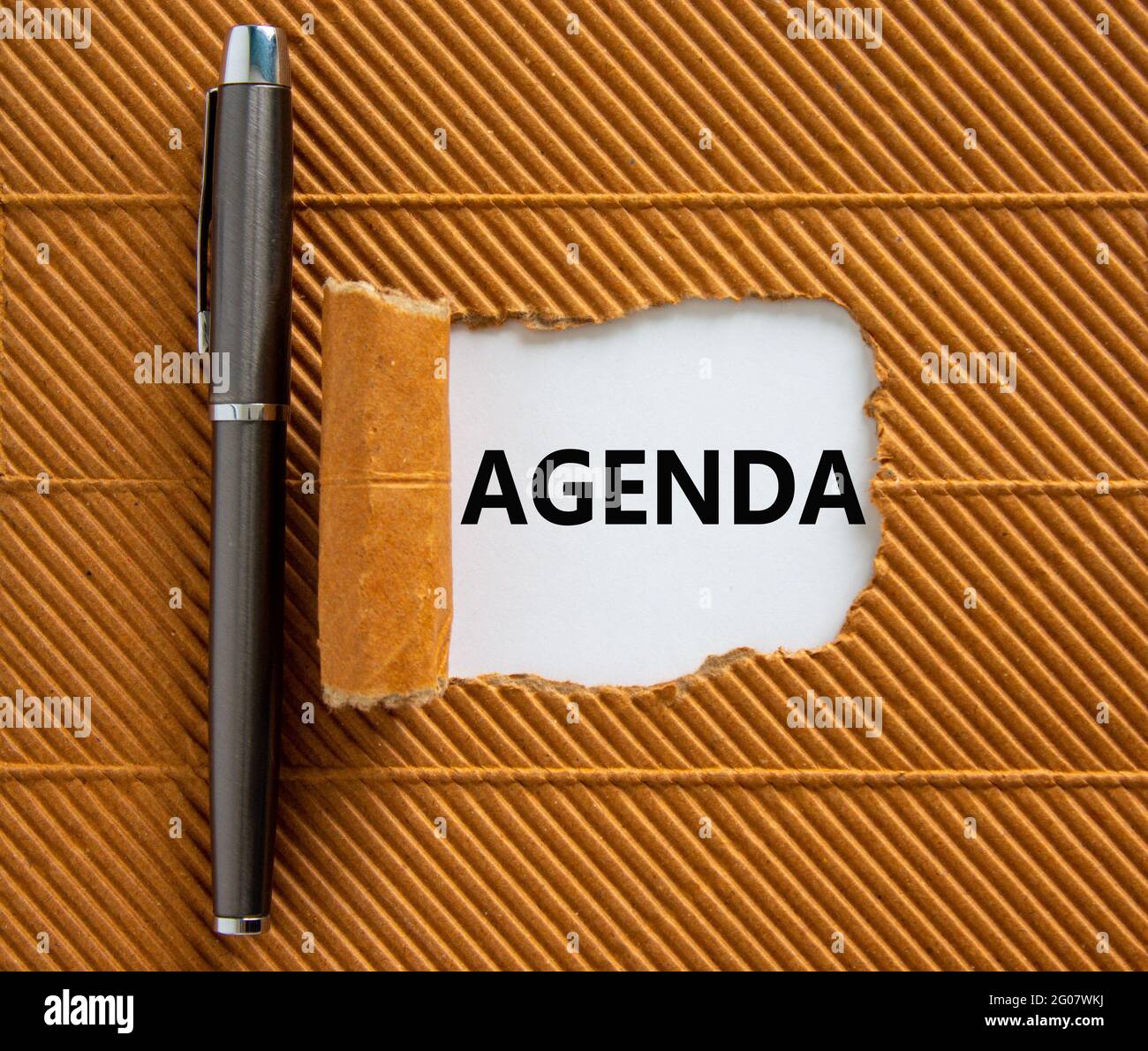 Symbole de l'entreprise et de l'ordre du jour. Le mot concept « agenda »  apparaît derrière un papier marron déchiré. Stylo métallique. Magnifique  arrière-plan marron, espace de copie. Affaires Photo Stock -