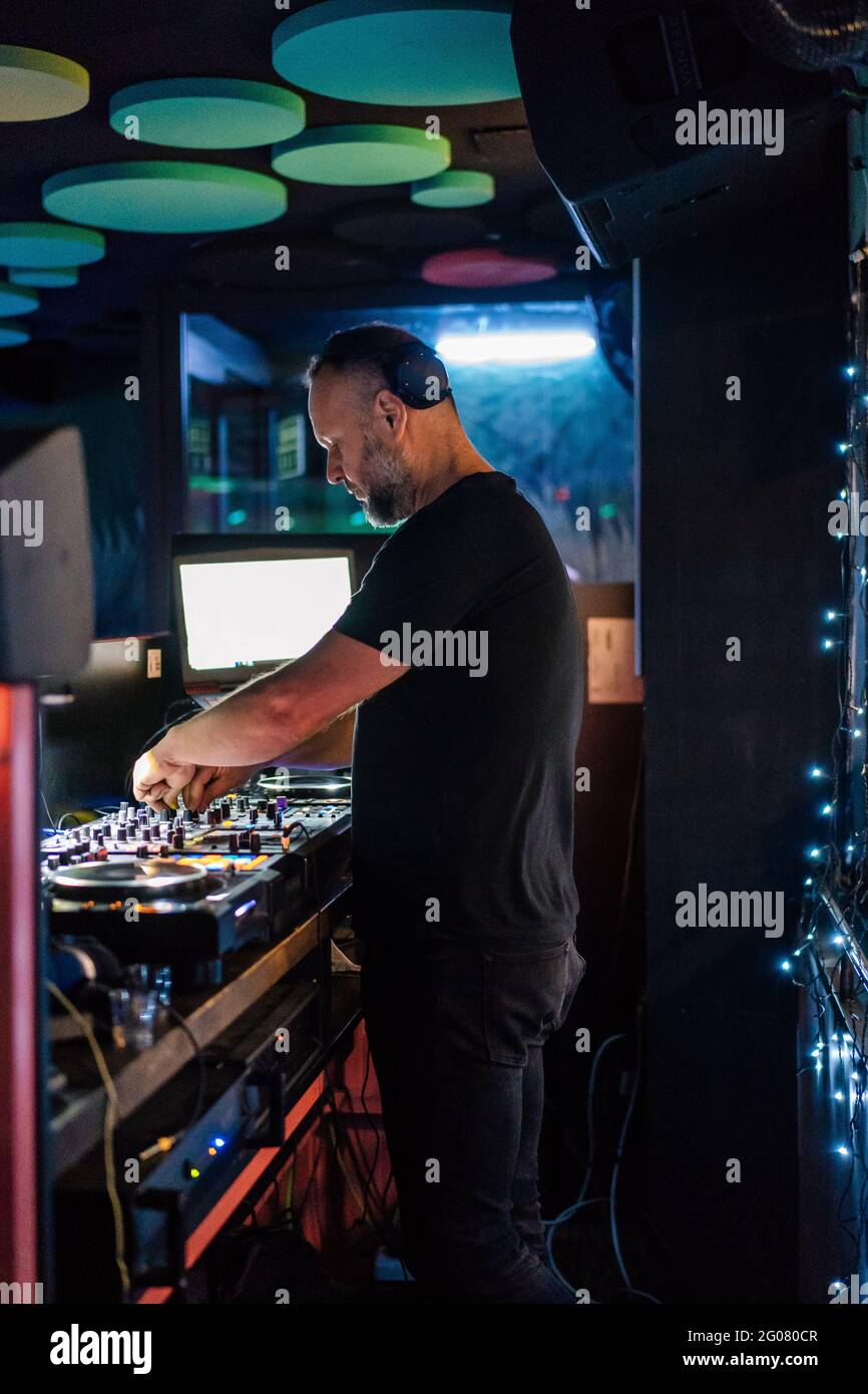 Vue latérale de l'homme d'âge moyen pensif en casque et noir Vêtements décontractés se concentrant et jouant DJ contrôleur professionnel pendant le spectacle au concert je Banque D'Images