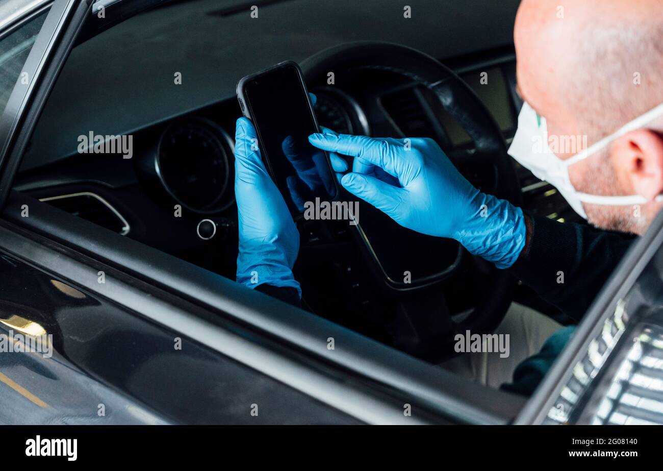 Vue latérale d'un homme sérieux utilisant un masque de protection assis en voiture pendant l'utilisation du téléphone portable pendant la période de quarantaine Banque D'Images