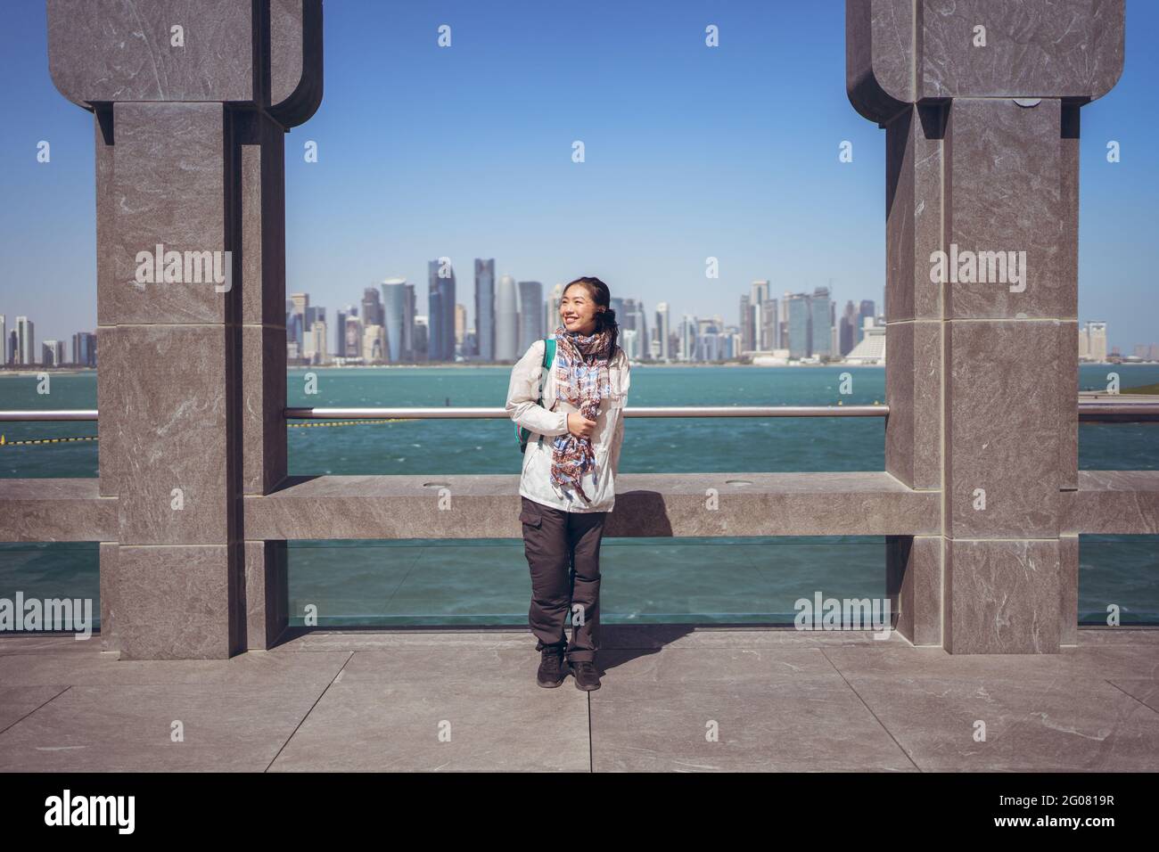 Vue de face d'une joyeuse asiatique touriste souriant à la caméra Tout en se tenant seul à côté de la clôture voûtée sur le front de mer dans le musée De l'art islamique contre nous Banque D'Images