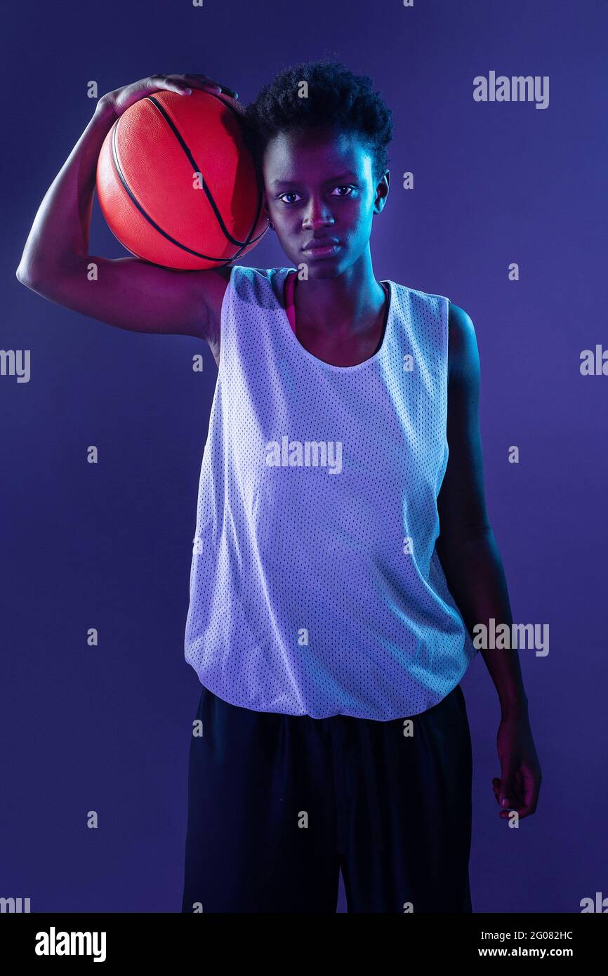 Femme noire avec tenue de basket ball dans le studio utilisant des gels de couleur et des projecteurs lumineux sur fond orange Photo Stock Alamy