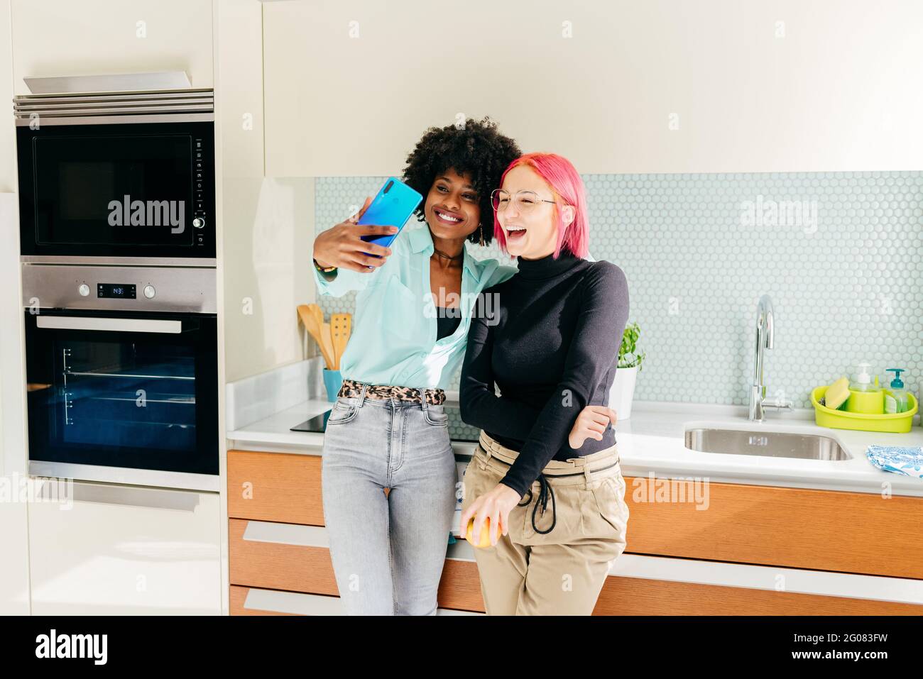 Des amies multiraciales stylées et joyeuses dans une tenue décontractée cuisine et prise de selfie avec téléphone portable Banque D'Images