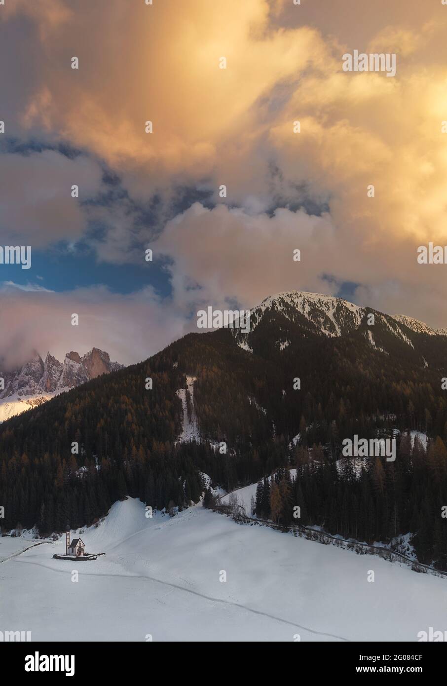 Église de Santa Maddalena avec d'épais nuages flottant sur des sommets de montagnes enneigées dans les Dolomites majestueuses, Italie. Banque D'Images