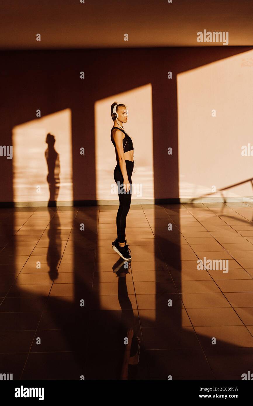 Jeune femme sportive de race blanche travaillant au coucher du soleil, à l'ombre et à la lumière sur l'arrière-plan Banque D'Images