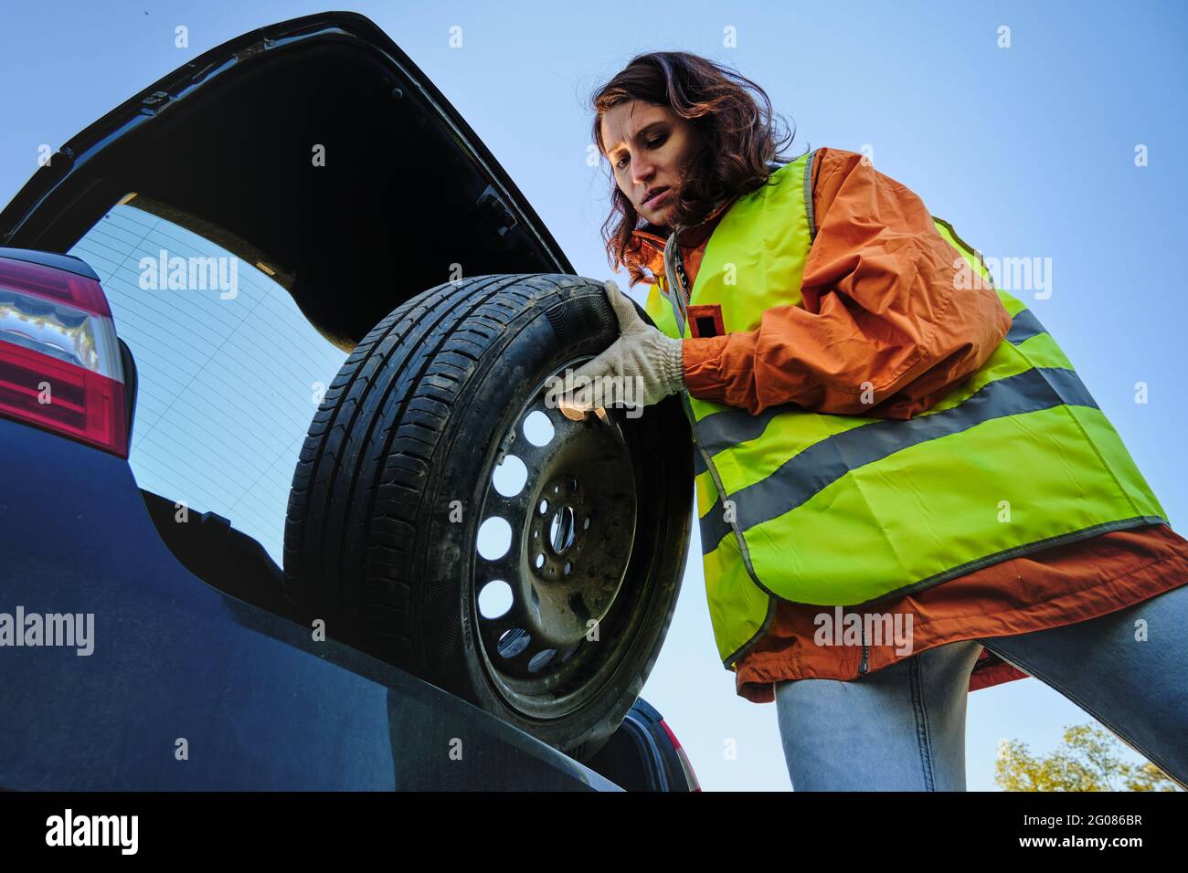 La fille change la roue endommagée de la voiture. Gilet vert. Roue de secours. Accident de la route. Voyagez en voiture. Banque D'Images