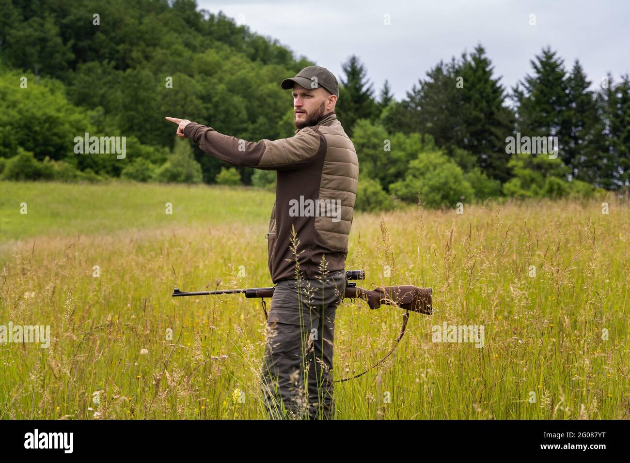 Jeune chasseur pointant une direction avec sa main tout en tenant un fusil de sniper Banque D'Images