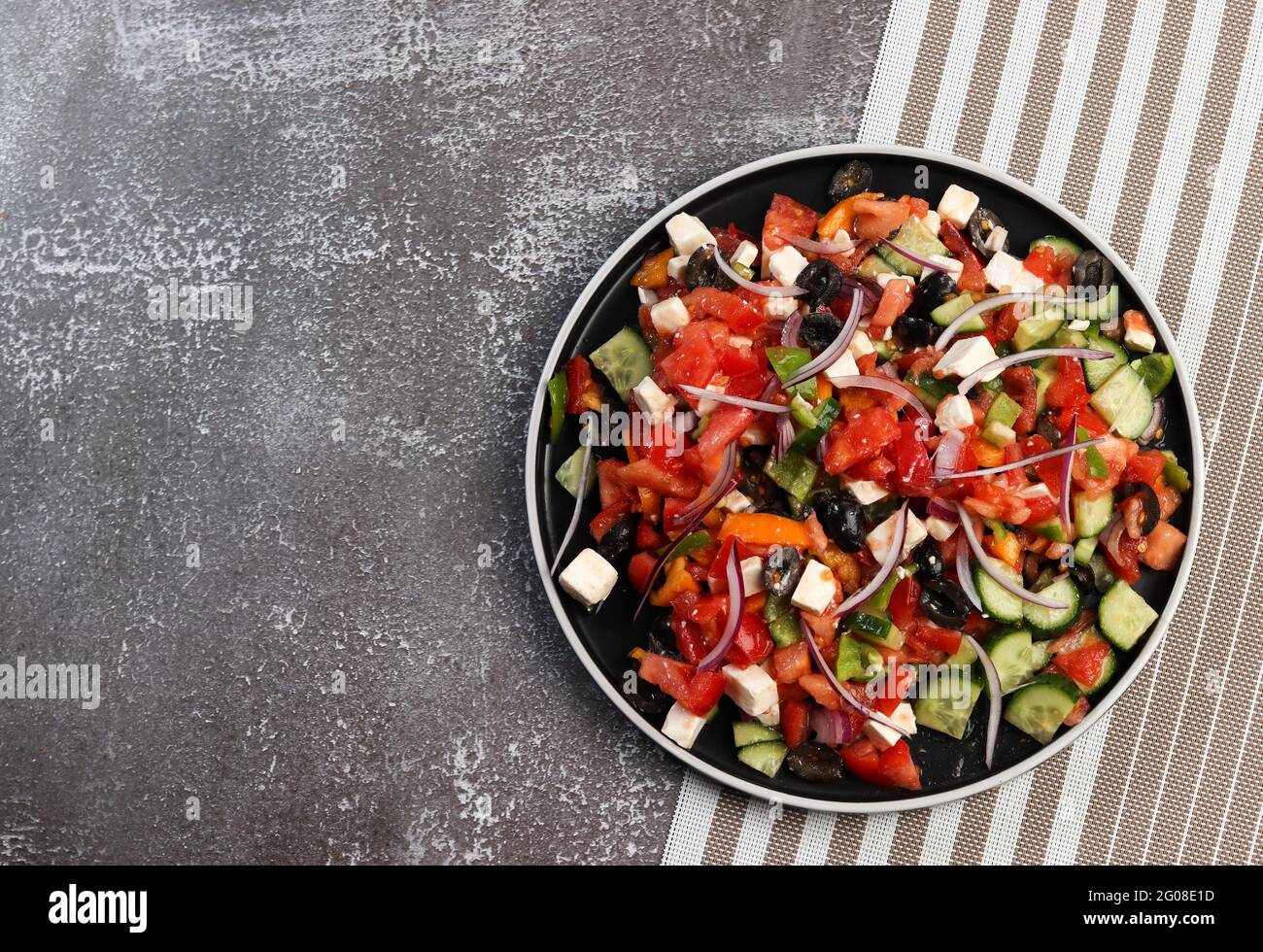 Salade grecque aux olives, tomates, concombres, oignons roses et feta sur une assiette ronde sur fond sombre. Vue de dessus, plan d'appartement Banque D'Images