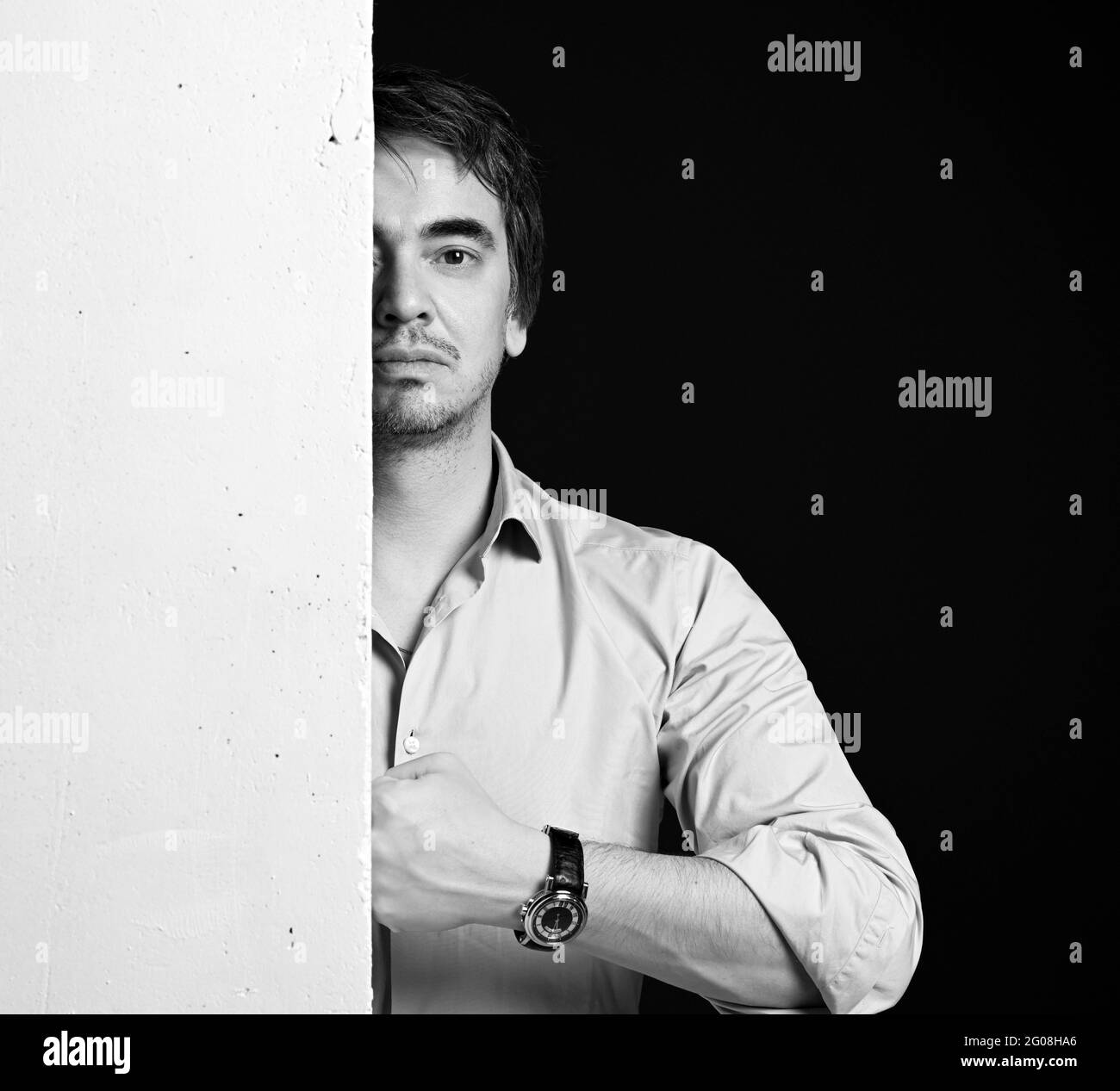 Portrait noir et blanc d'un homme d'âge moyen en chemise debout derrière un mur de béton blanc et claquant son poing Banque D'Images
