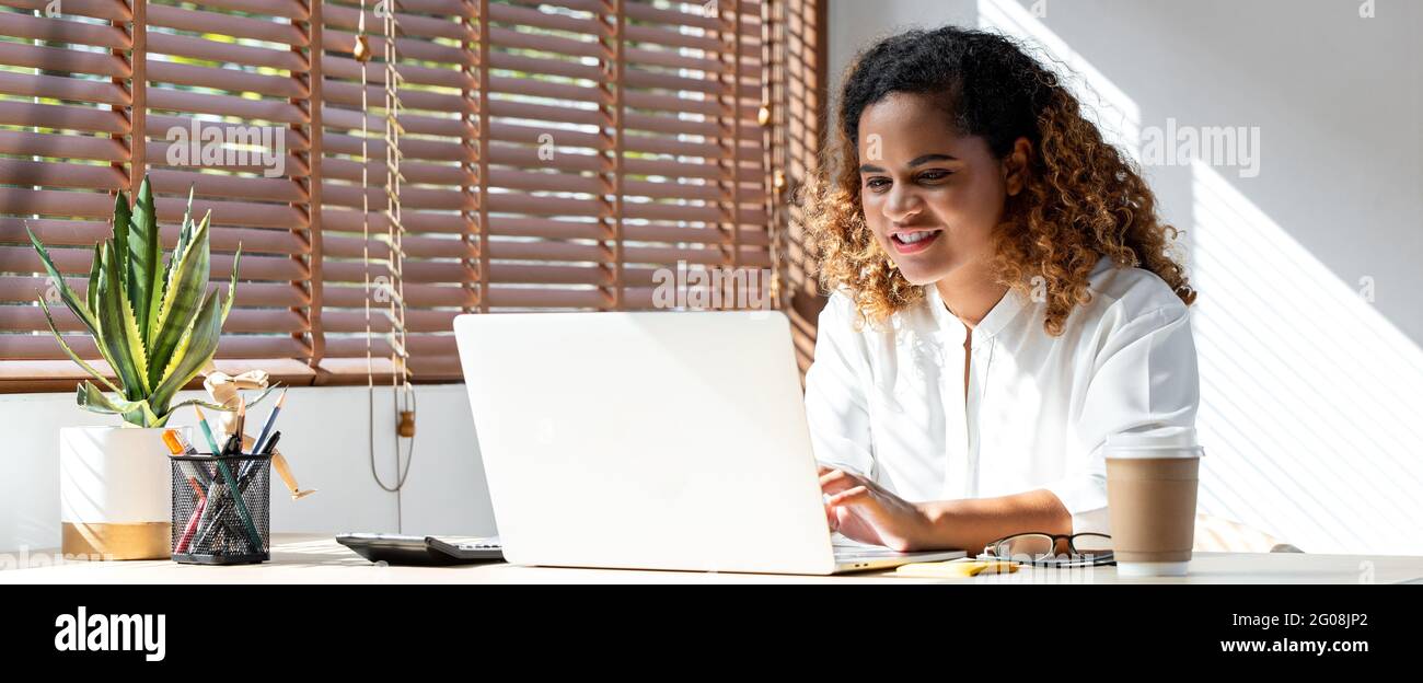 Photo de bannière d'une jeune femme d'affaires afro-américaine heureuse travaillant à domicile sur un ordinateur portable dans le salon Banque D'Images