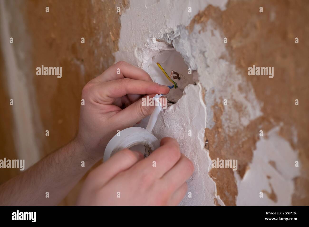 Gros plan d'un électricien qui met deux câbles ensemble et y ajoute du ruban isolant Banque D'Images