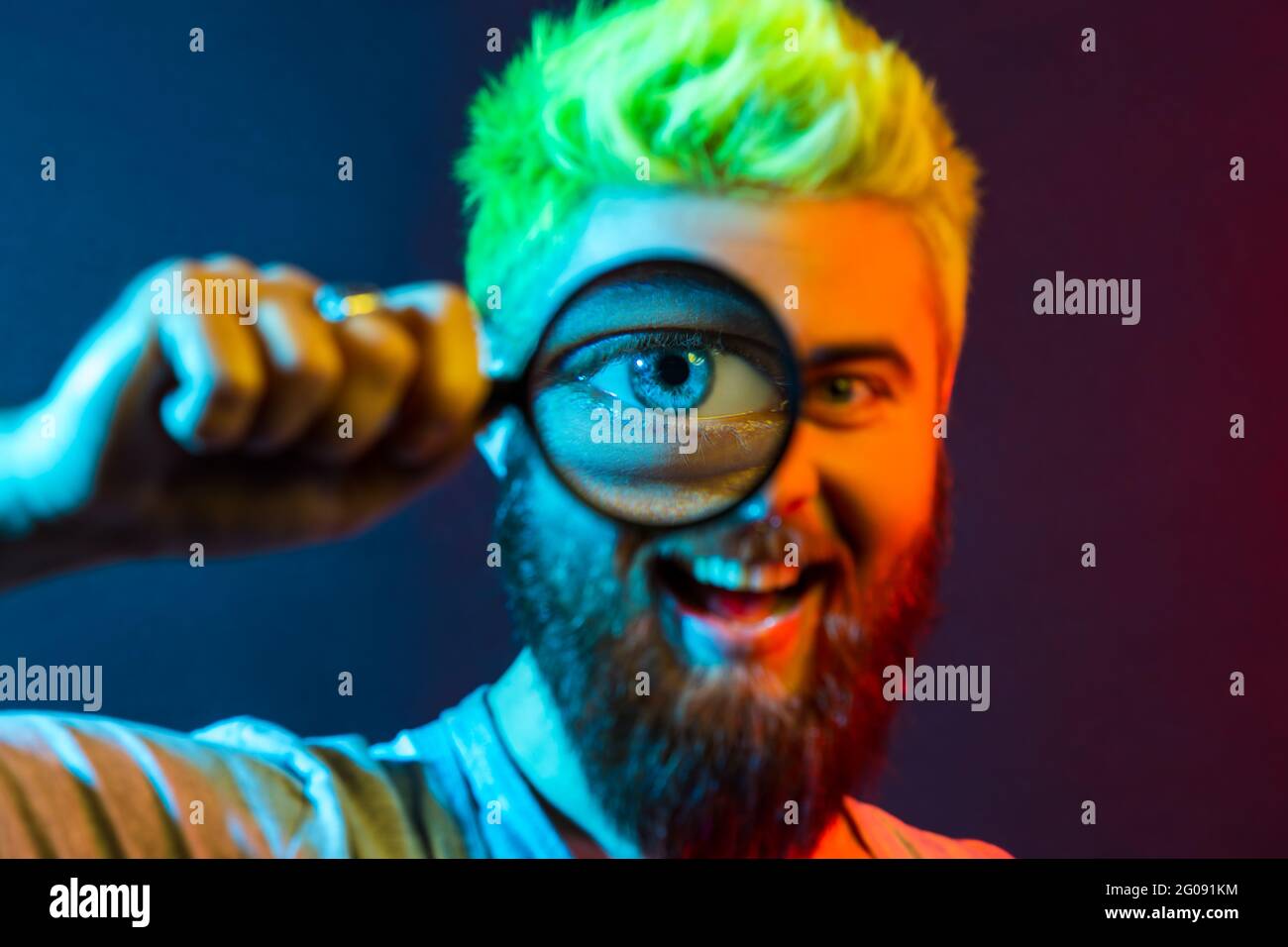 Portrait d'un jeune homme adulte heureux dans une combinaison en denim tenant une loupe et regardant l'appareil photo avec un grand œil zoom, un visage joyeux et un sourire ensanglant. Co Banque D'Images Portrait d'un jeune homme adulte heureux dans une combinaison en denim tenant une loupe et regardant l'appareil photo avec un grand œil zoom, un visage joyeux et un sourire ensanglant. Co Banque D'Images