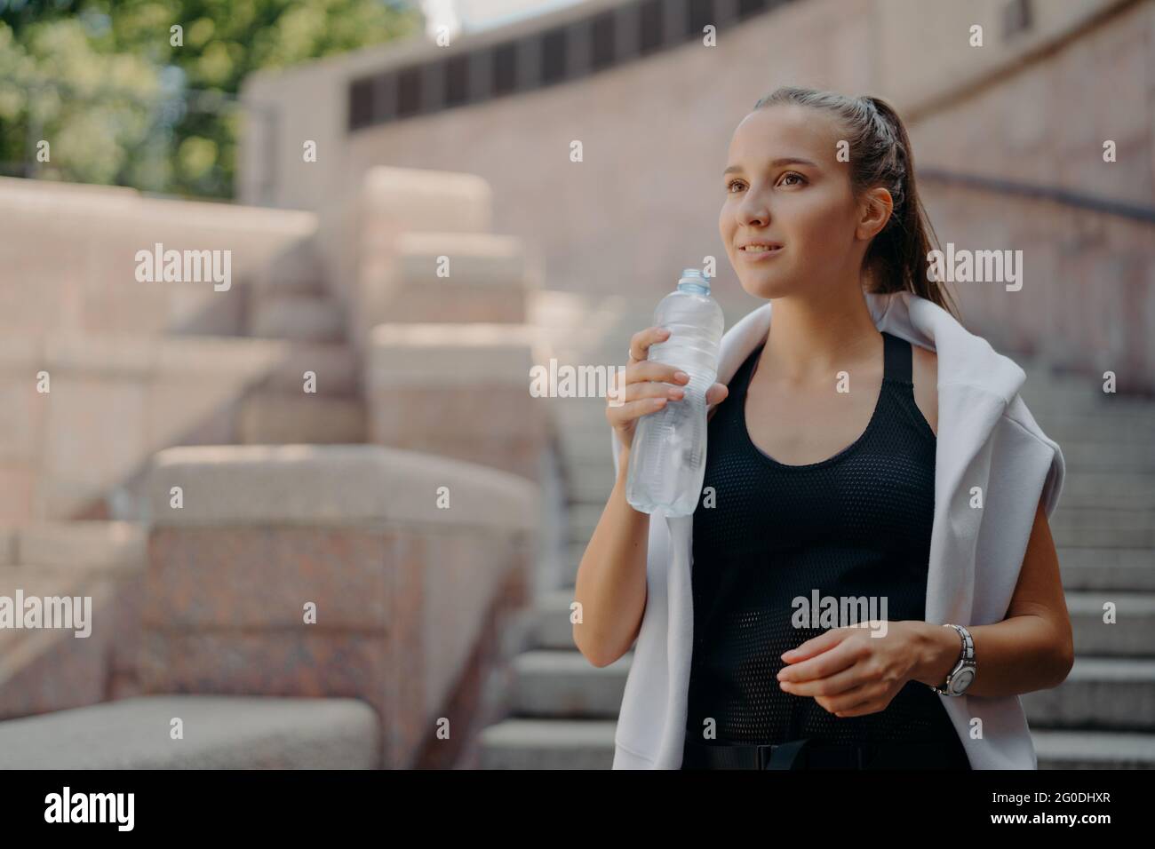Femme avec se sent soif après l'entraînement cardio boissons eau de bouteille tient boisson rafraîchit reste hydraté poses dehors vêtu de vêtements actifs Banque D'Images