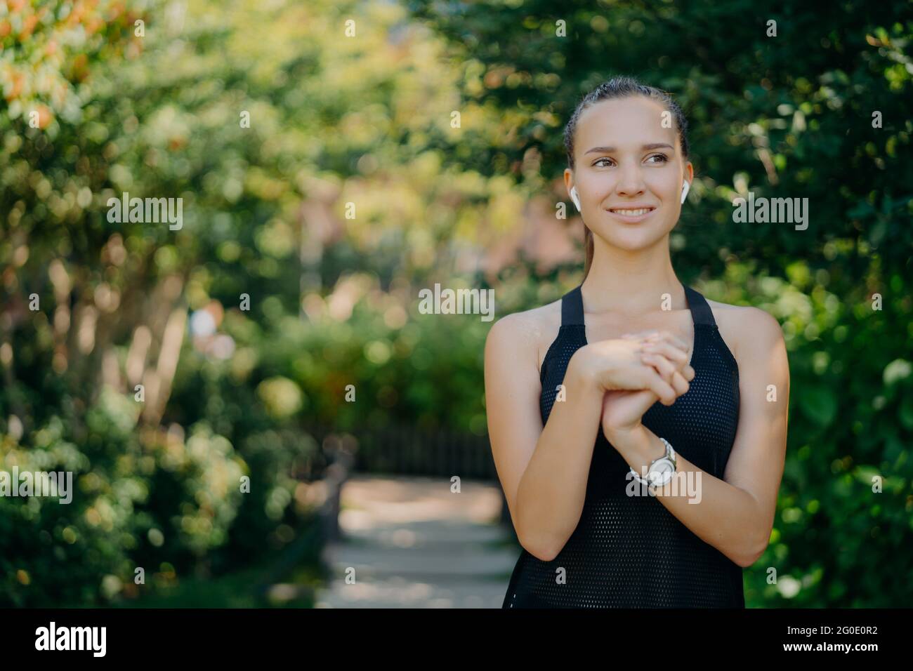 Active femme sportive avec les cheveux foncés la peau saine garde les mains ensemble prépare pour l'entraînement centré sur la distance sourires heureux apprécie la nature et Banque D'Images