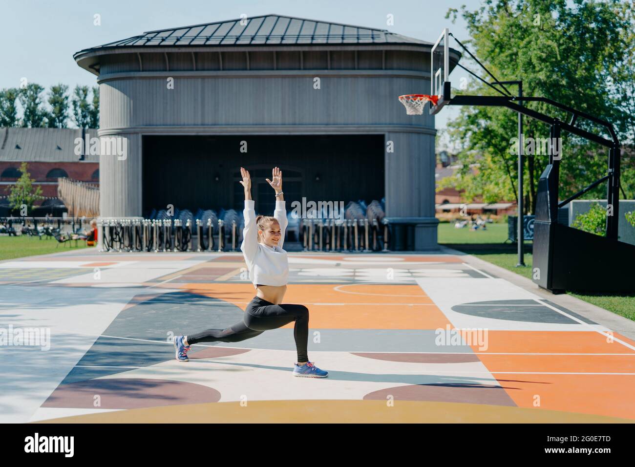 Une femme sportive fait des exercices physiques à l'extérieur garde les bras levés se réchauffe avant de courir vêtus de poses de vêtements actifs sur le terrain de basket-ball Banque D'Images