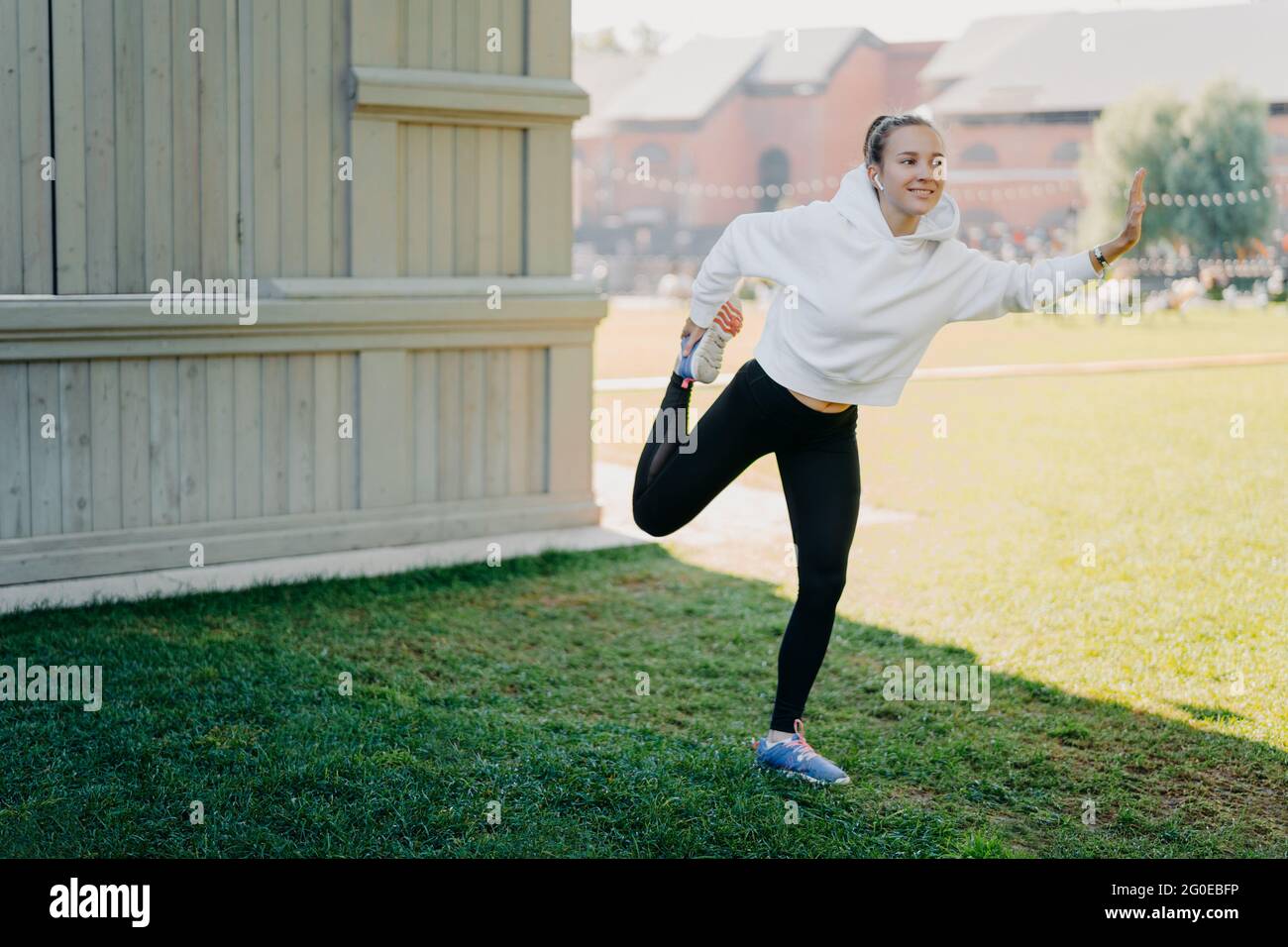 Une jeune femme active et heureuse à capuche et leggings se prépare pour les corches de course à pied et réchauffe les jambes focalisées sur la distance écoute de la musique via Banque D'Images
