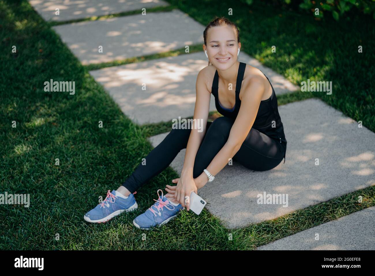 Positive a le repos après l'entraînement actif utilise smartphone heureux d'atteindre l'objectif de forme physique partage le contenu dans le blog vêtu de vêtements actifs sourires agréablement Banque D'Images
