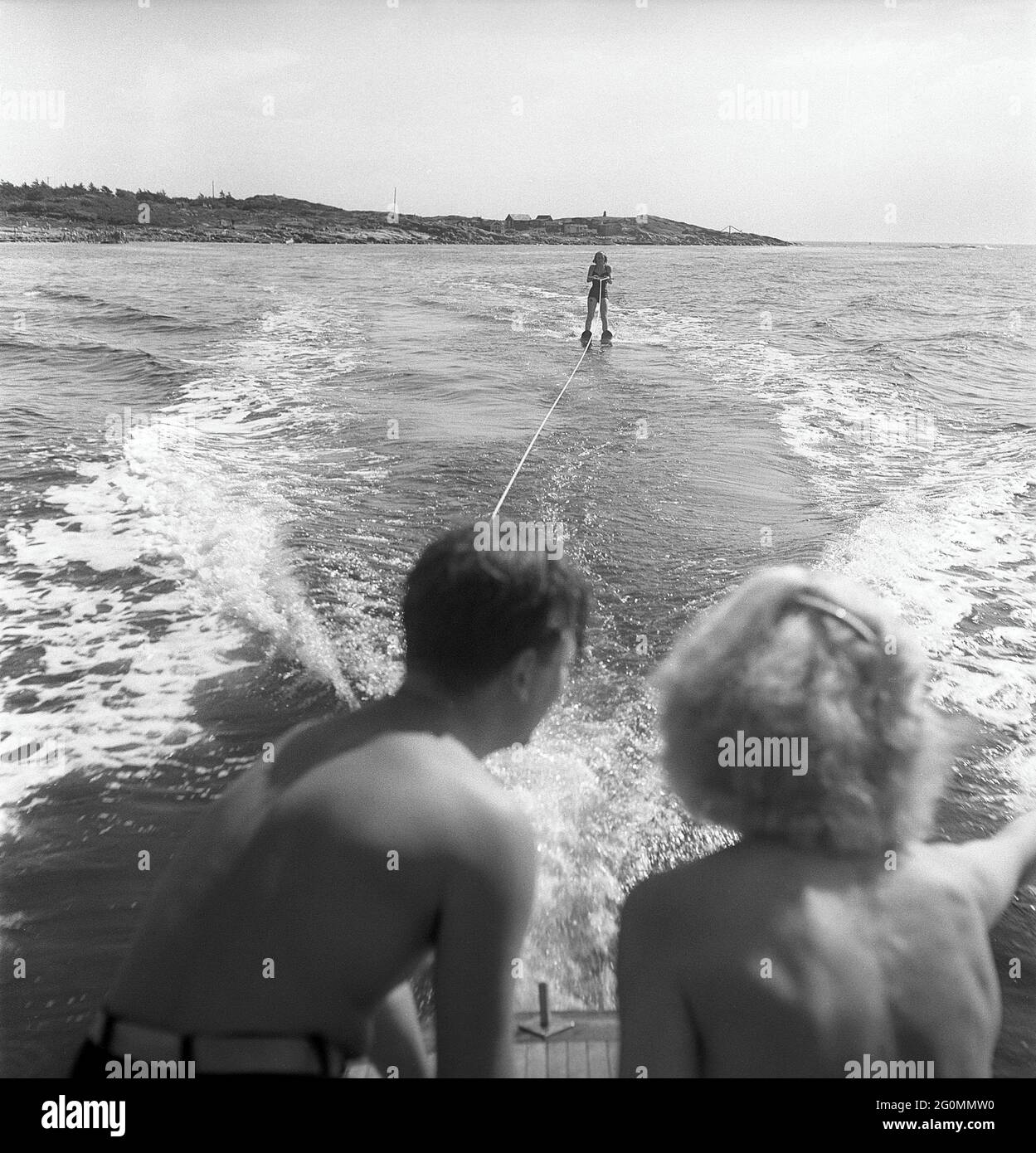 années 1950 sur la plage. Une jeune femme en bord de mer essaie le sport nautique relativement nouveau, le ski nautique. Elle a réussi à maîtriser l'art du ski nautique et est vue ici sur son skiis qui commande le bateau à moteur. Suède 1952. Réf. BD4-8 Banque D'Images