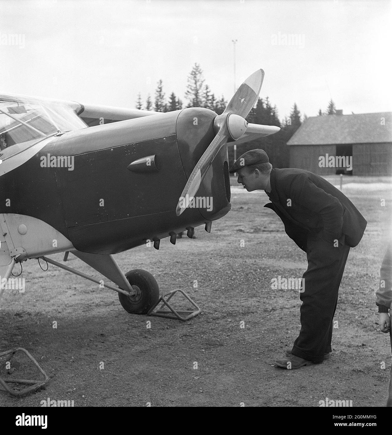 Avion dans les années 1950. Un homme est debout à côté d'un petit avion et est curieux de voir ce qui est à l'intérieur. Il regarde bien devant l'avion. Selon la légende originale de la photo, il est sceptique d'être un passager sur le petit avion qu'il pense pas en sécurité. Suède 1952 réf. AY40-4 Banque D'Images