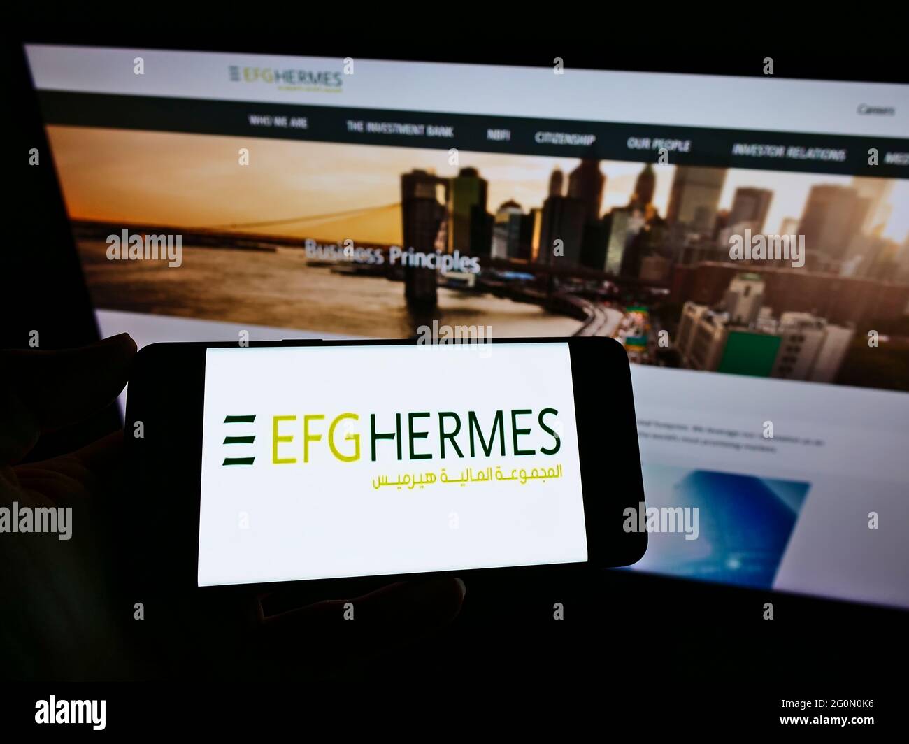 Personne tenant un téléphone portable avec le logo de la société financière égyptienne EFG Hermes Holding SAE sur l'écran en face de la page web. Mise au point sur l'affichage du téléphone. Banque D'Images