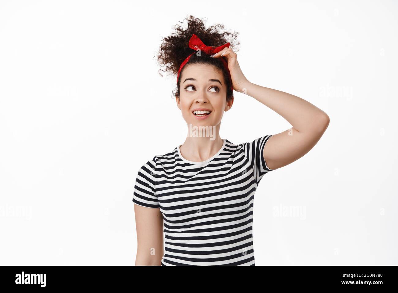 Portrait de la tête de grattage de fille brunette réfléchie, regardant vers le haut et la tête de grattage, pensant, à la recherche d'idées ou d'inspiration, debout contre blanc Banque D'Images