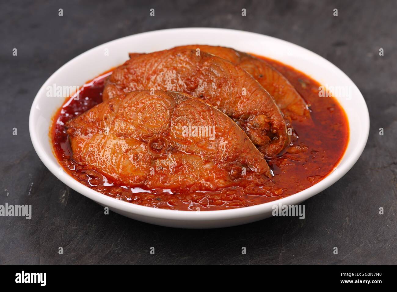 Séer curry de poisson, curry traditionnel de poisson indien, arrangé dans un bol en céramique blanc sur un fond gris texturé, isolé. Banque D'Images